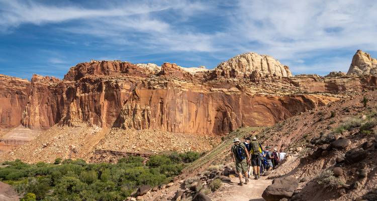 Hikers walking along a trail surrounded by red cliffs and blue sky.