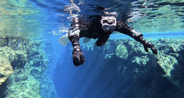 Buceador explorando formaciones rocosas submarinas con agua azul cristalina.