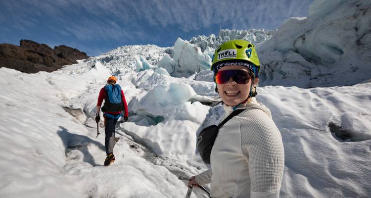 Des aventuriers munis de casques et de piolets traversant un glacier brillant sous un ciel bleu.
