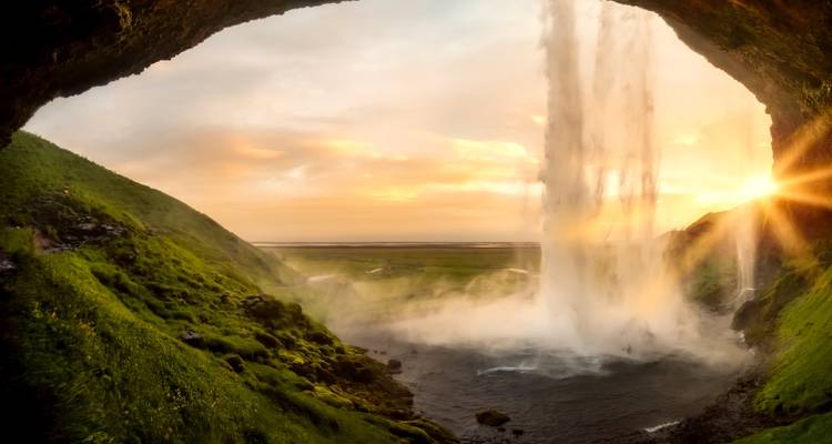 La lumière du coucher de soleil traverse la cascade de Seljalandsfoss en créant une brume et une lueur dorée sur la plaine islandaise.