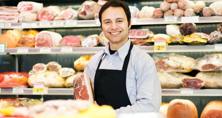 Boucher souriant, tenant un morceau de viande dans un magasin.