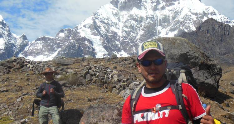 Wandelaars in bergachtig terrein met besneeuwde toppen op de achtergrond.