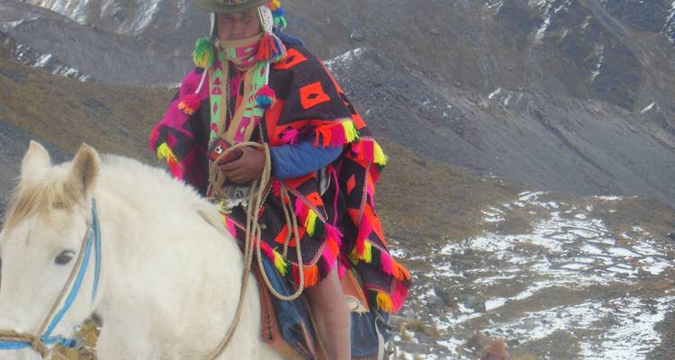 Kleurrijk geklede persoon op een paard in een bergachtig gebied.