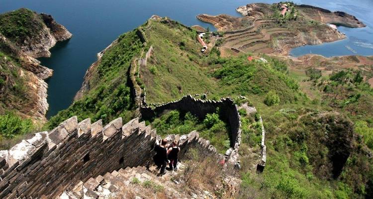 Parte de la Gran Muralla China a lo largo de un cuerpo de agua, con visitantes caminando.