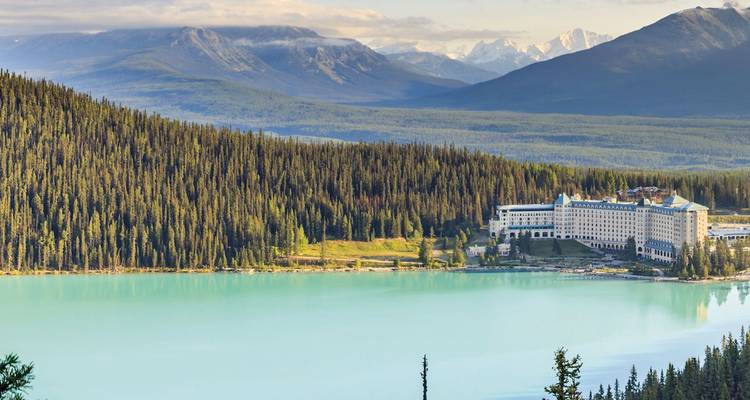El lago turquesa Louise con el Fairmont Chateau acurrucado debajo de montañas boscosas y picos nevados a lo lejos