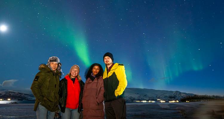 Groupe de voyageurs emmitouflés posent sous l'aurore boréale verte scintillante dans le nord neigeux de la Norvège