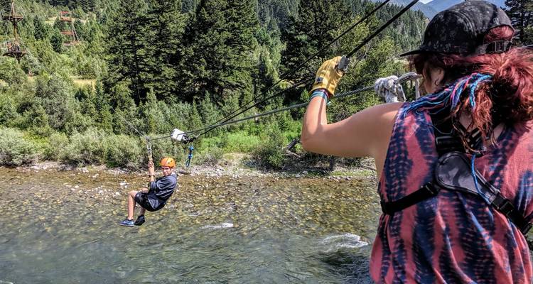 Een persoon die aan een zipline over een rivier gaat met bomen op de achtergrond.