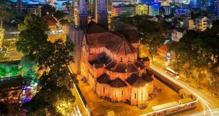 Nächtliche Luftaufnahme der roten Backsteinkathedrale Saigon Notre-Dame, umgeben von Lichtspuren in Ho-Chi-Minh-Stadt.