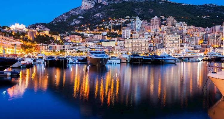 Puerto de Mónaco con numerosos barcos y edificios bien iluminados reflejándose en el agua.