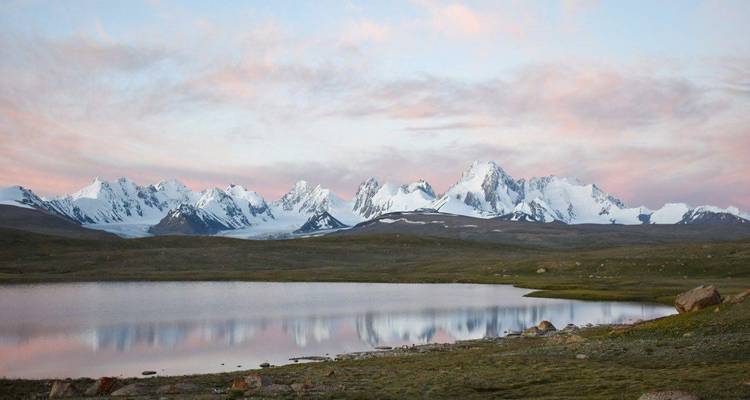 Atemberaubender Blick auf verschneite Berge, die sich bei Sonnenuntergang in einem ruhigen See spiegeln.