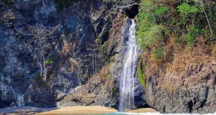 Cascade plongeant d'une falaise rocheuse sur une crique de sable isolée