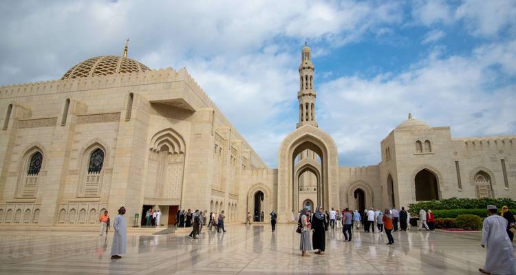 Mezquita blanca con cúpulas y minaretes bajo un cielo nublado.