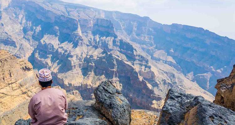Person, die auf Felsen sitzt und Berge und Täler überblickt.