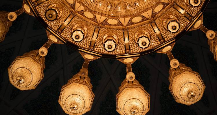 Lujoso candelabro colgando de un techo ricamente decorado en una habitación poco iluminada.