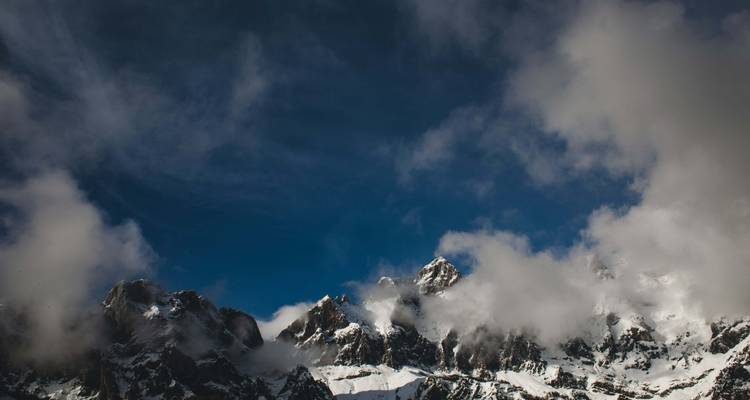 Schneebedeckte Berggipfel, die teilweise von Wolken verdeckt sind.