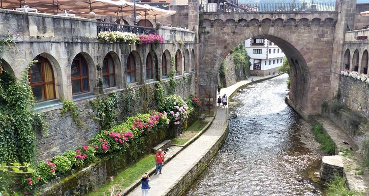 Pont historique en pierre au-dessus d'une rivière avec des fleurs et des gens.