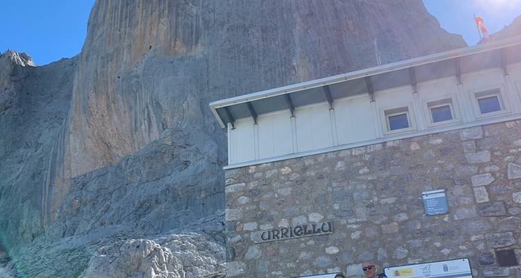 Refuge avec falaise rocheuse et ciel bleu, vue partielle d'alpinistes.
