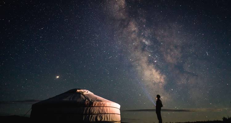 Una persona silueteada contra un cielo estrellado con una yurta en primer plano.