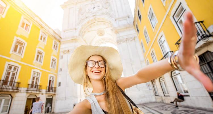 Touriste pose avec un chapeau à large bord et des bâtiments colorés derrière.