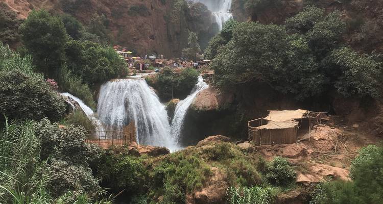 Waterfalls surrounded by lush greenery, with people and market stalls at the top.