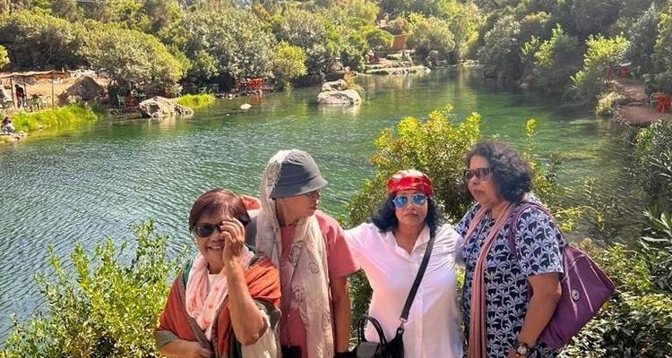 Four women posing by a river surrounded by greenery.
