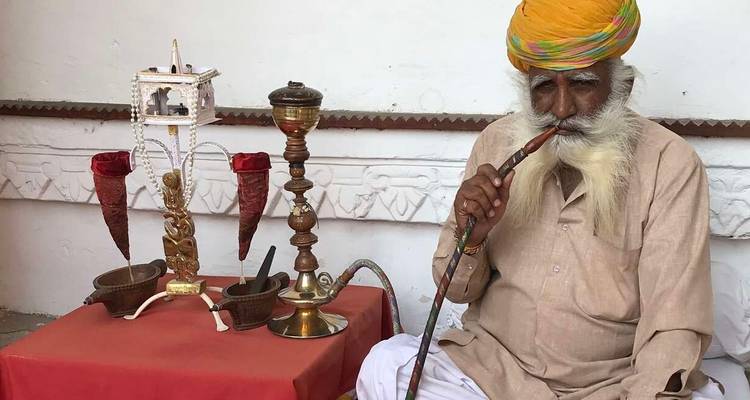 Un homme âgé assis fumant une chicha en tenue traditionnelle.