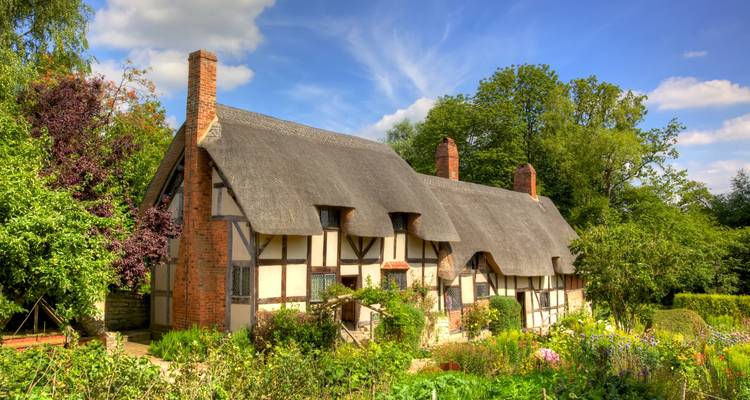 Thatched cottage surrounded by lush gardens in Stratford-upon-Avon, England.