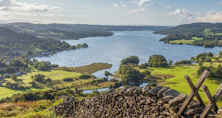 Vue panoramique sur les collines verdoyantes et le lac Windermere avec des nuages épars et le soleil de fin de journée.