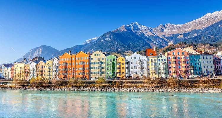 Colorful buildings along the river in Innsbruck with mountains in the background.