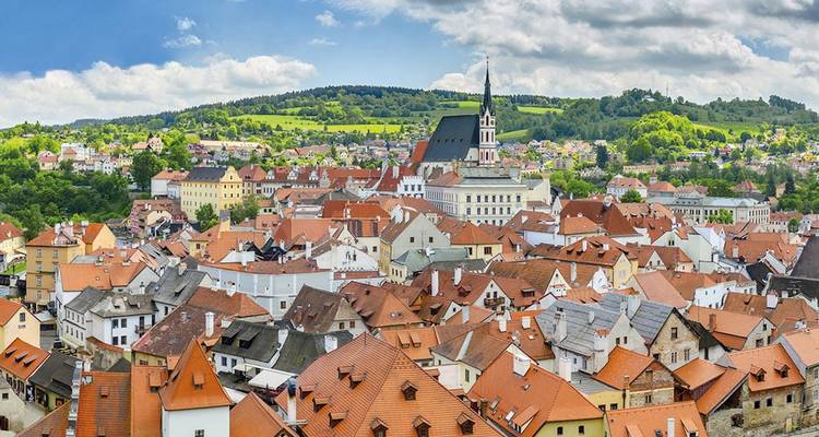 Panoramablick auf die roten Ziegeldächer von Cesky Krumlov und den Kirchturm inmitten grüner Hügel