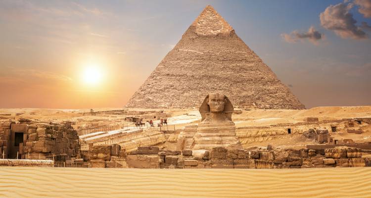 El sol se pone detrás de la Gran Pirámide iluminando con un brillo cálido la Esfinge y el desierto arenoso del primer plano.