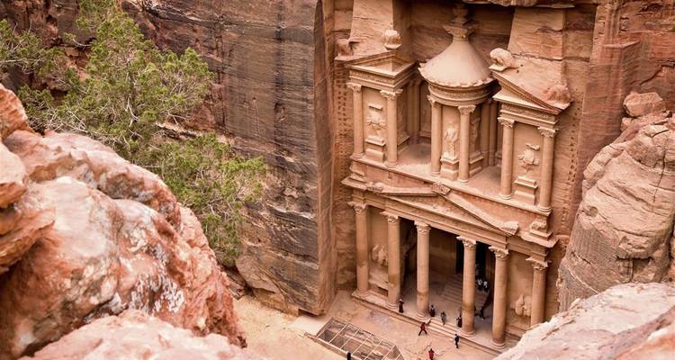 Vista elevada del Tesoro de Petra tallado en acantilados de color rojo rosado con pequeños visitantes en su base.