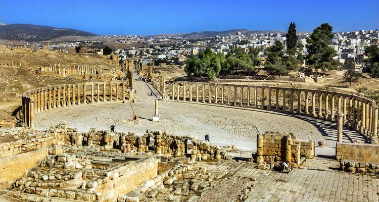 Foro ovalado antiguo y calles con columnas del sitio arqueológico de Jerash con la ciudad moderna de fondo.