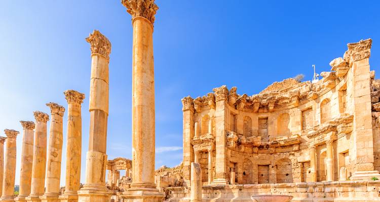 Columnas iluminadas por el sol y ruinas del teatro de piedra de Jerash contra un vibrante cielo azul jordano.