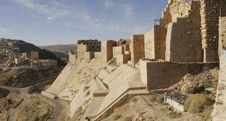 Los muros y murallas de piedra del Castillo de Kerak se extienden a lo largo de una ladera empinada que domina un camino sinuoso.