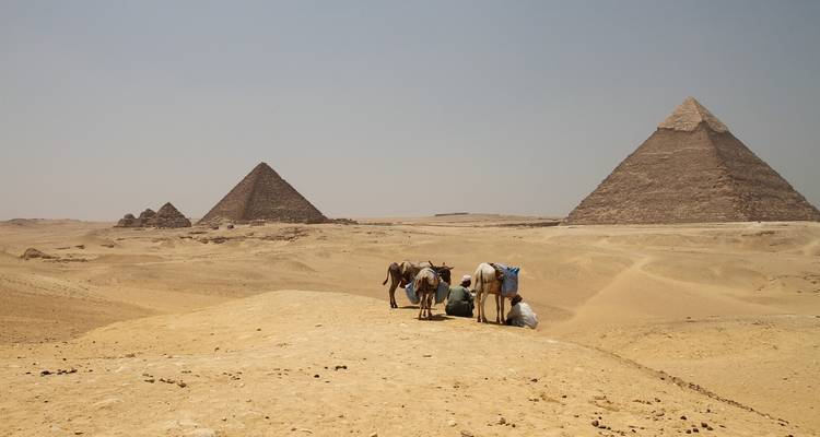 Esel mit Reitern hielten auf Dünen an und blickten auf die entfernten Pyramiden von Giza unter dem diesigem Mittagslicht.