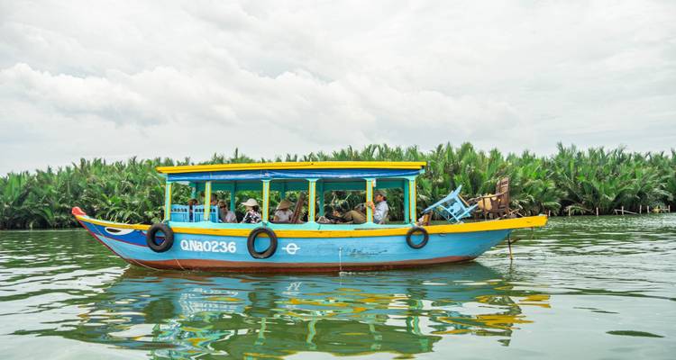 Buntes Boot auf einem Fluss mit Passagieren, umgeben von üppiger Vegetation.