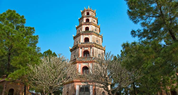 Pine trees surround the Pagoda of Thien Mu Temple under a clear blue sky.