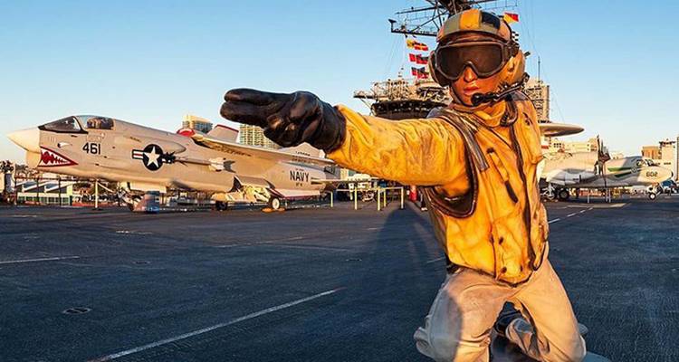 Aviation officer on an aircraft carrier deck with fighter jets in the background.