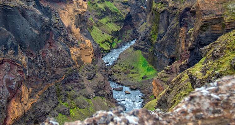 Cañón profundo y estrecho con un río sinuoso en el fondo, paredes de roca estratificadas de colores y manchas de musgo.