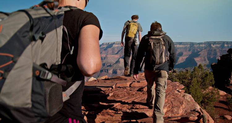 Plano cerrado de excursionistas con mochilas caminando en un borde rocoso sobre un cañón enorme