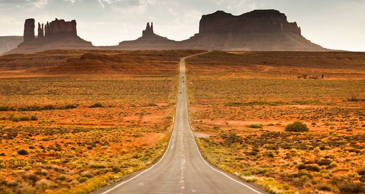 Carretera larga y recta del desierto que lleva hacia los monumentales buttes en el horizonte