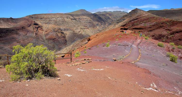 Rocky terrain with red and brown earth and distant mountains.