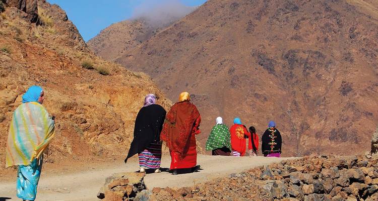 Grupo de mujeres con atuendo colorido caminando por un sendero de montaña.