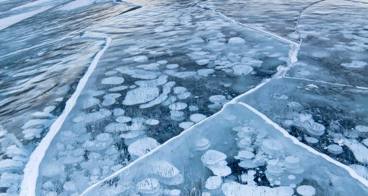 Gros plan de bulles de méthane gelé emprisonnées sous la glace de lac translucide et fissurée.