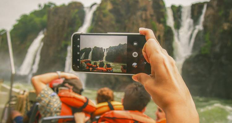 Des personnes sur un bateau prenant des photos d'une cascade avec un smartphone.