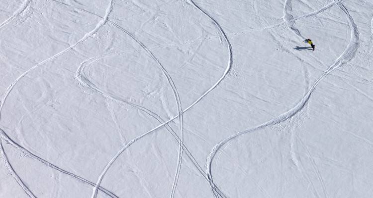 Luftaufnahme eines einzelnen Skifahrers, der frische Spuren über ein unberührtes Schneefeld zieht.