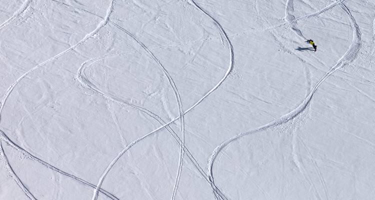 Vue aérienne d'un vaste champ de neige marqué par d'élégantes traces de ski avec un skieur solitaire traçant de nouveaux virages.