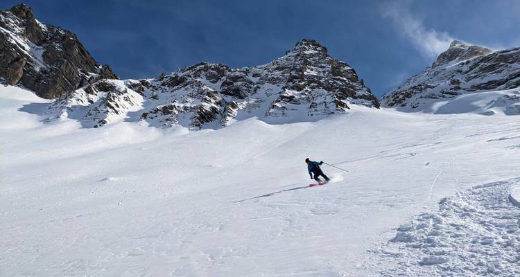 Skifahrer, der eine steile Pulverhang unter ragenden Alpengipfeln hinunterfährt.