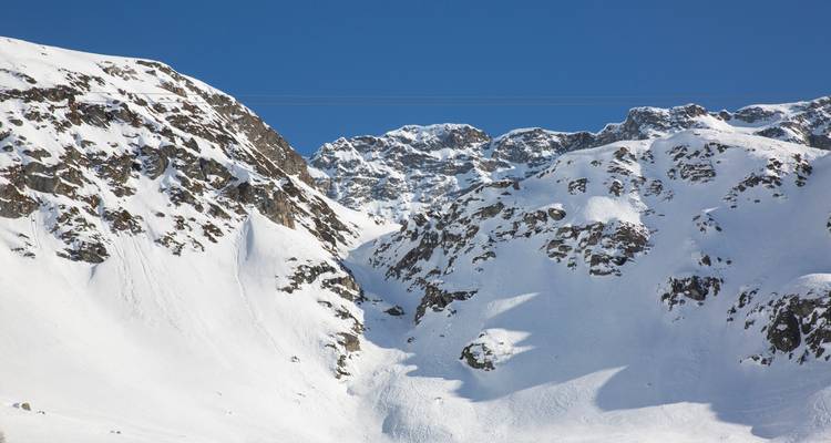 Nahaufnahme von rauen, schneebedeckten Felsflanken unter einem klaren, blauen Alpenhimmel.